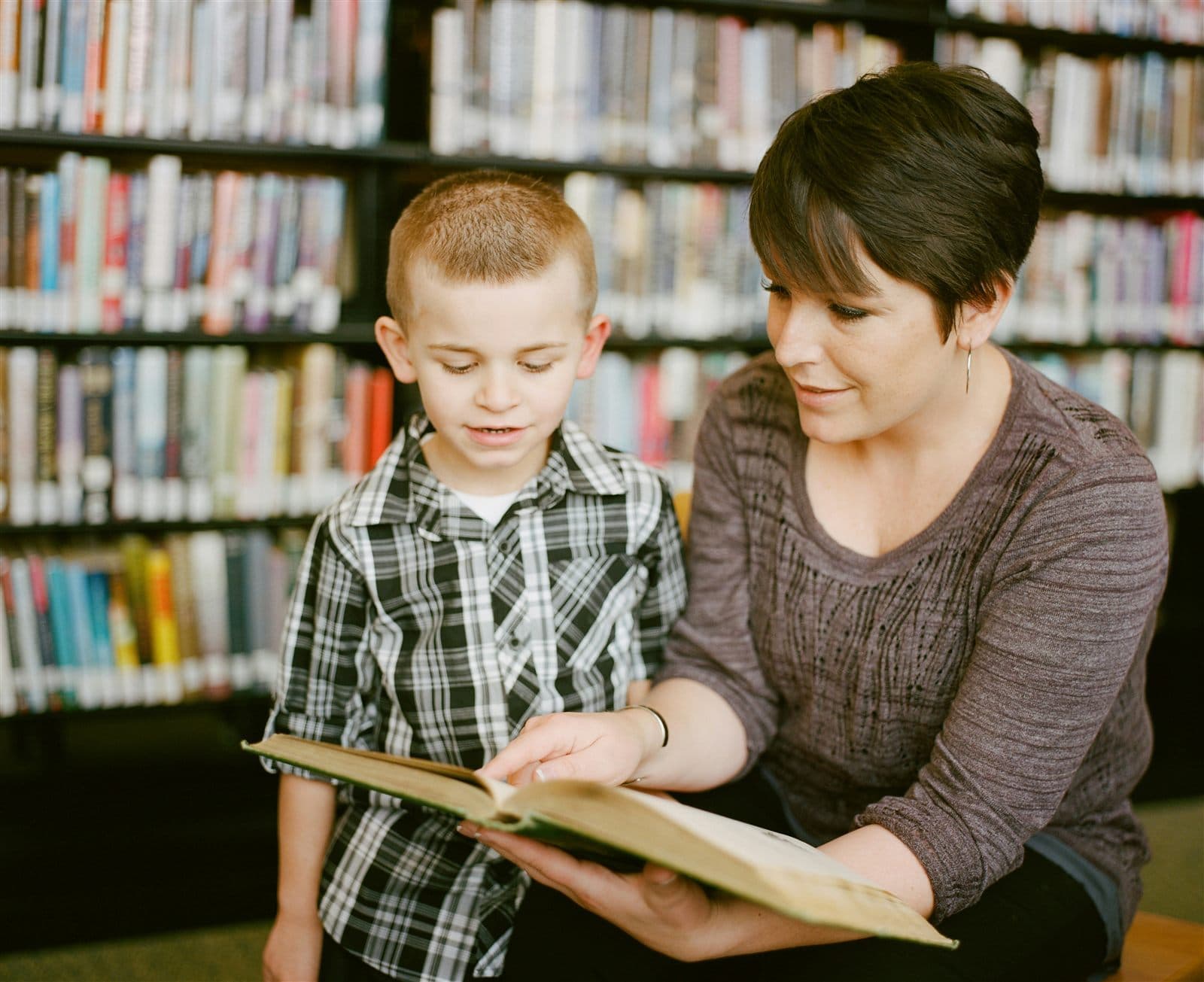 A mother smiling as she reads with her happy, engaged son